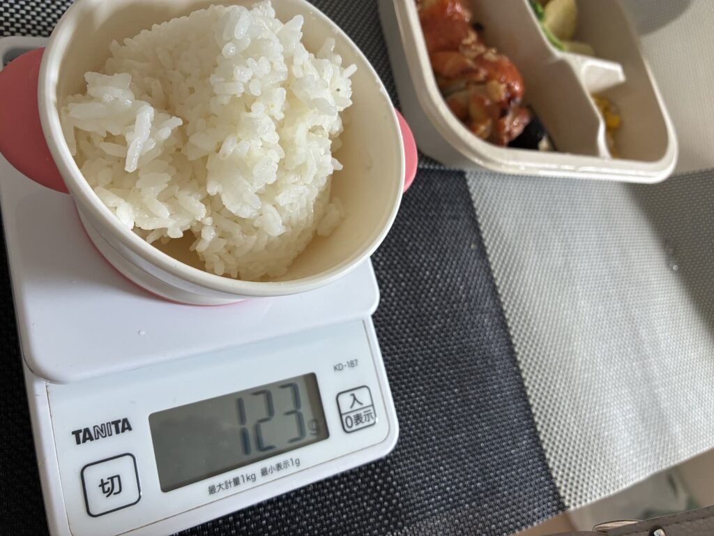 はかりにのせたご飯と、トマトガーリックチキンステーキのデリ弁当
