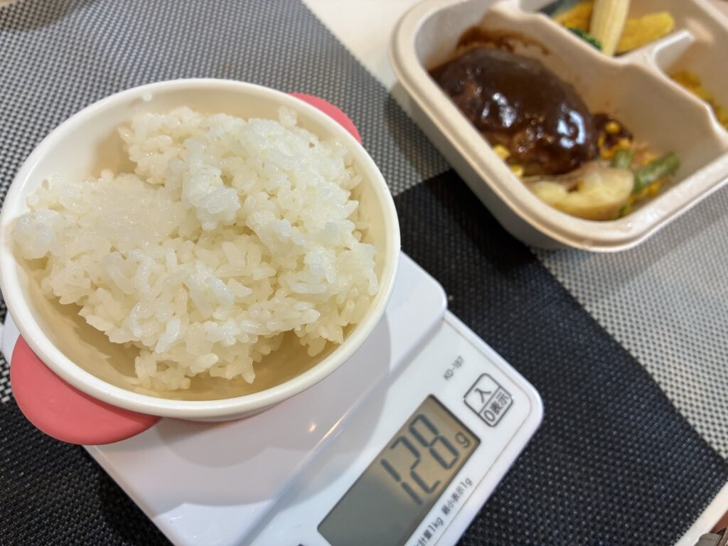 はかりにのせたご飯と、デミグラスハンバーグのデリ弁当